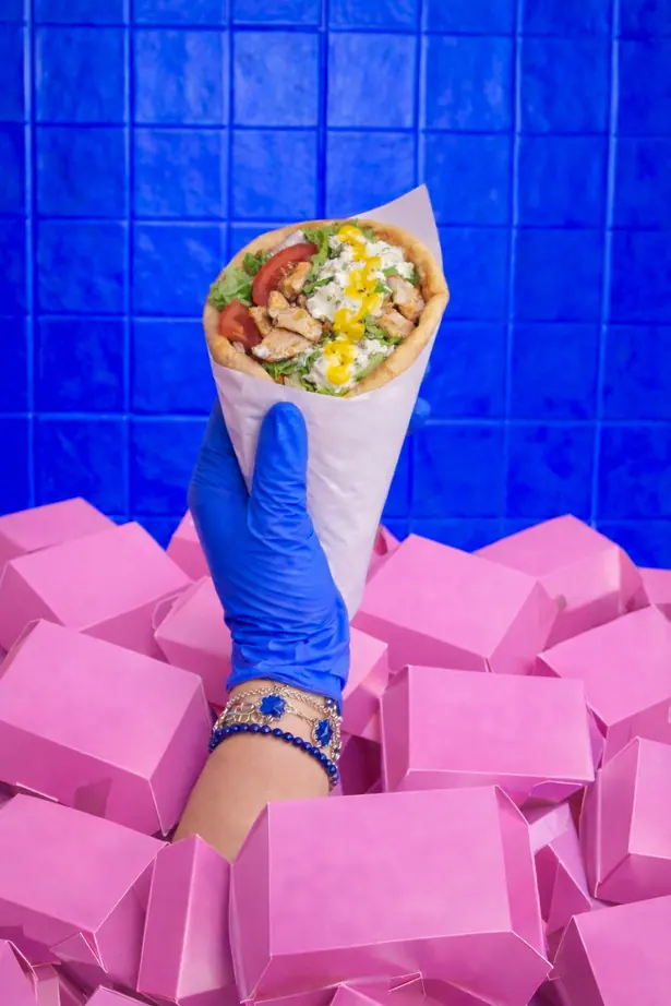 Une pita grecque garnie, tenue sur fond de barquettes roses